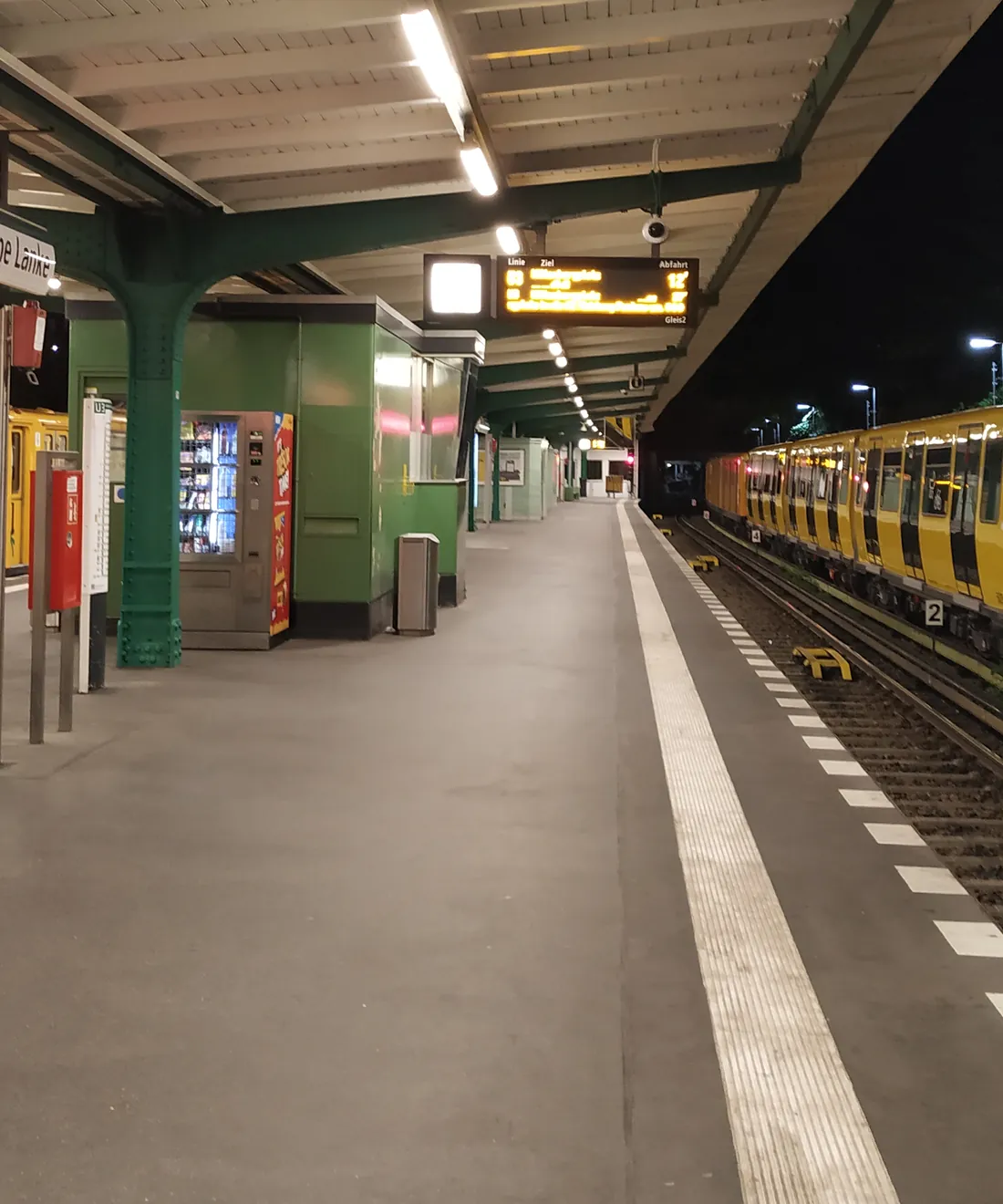 An illuminated platform and a yellow U-Bahn train at Krumme Lanke station in Berlin at night.